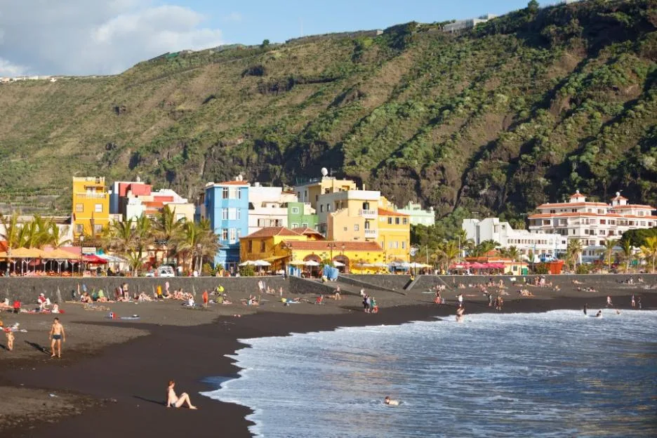 Colorful Puerto de Tazacorte with tourists sunbathing on the dark beach.