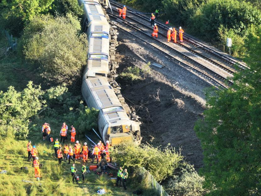 Overhead view of a train derailment with emergency personnel inspecting the scene.
