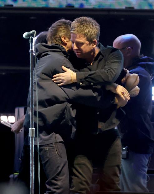 Liam and Noel Gallagher embracing on stage during an Oasis performance.