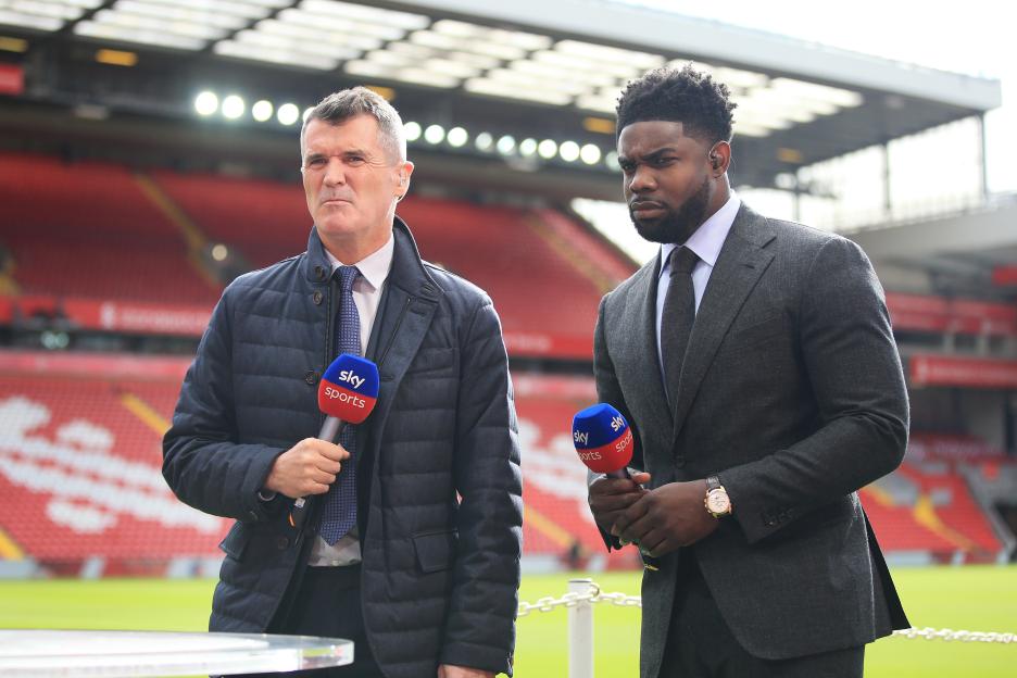 Sky Sports pundits Roy Keane and Micah Richards holding microphones at a soccer match.