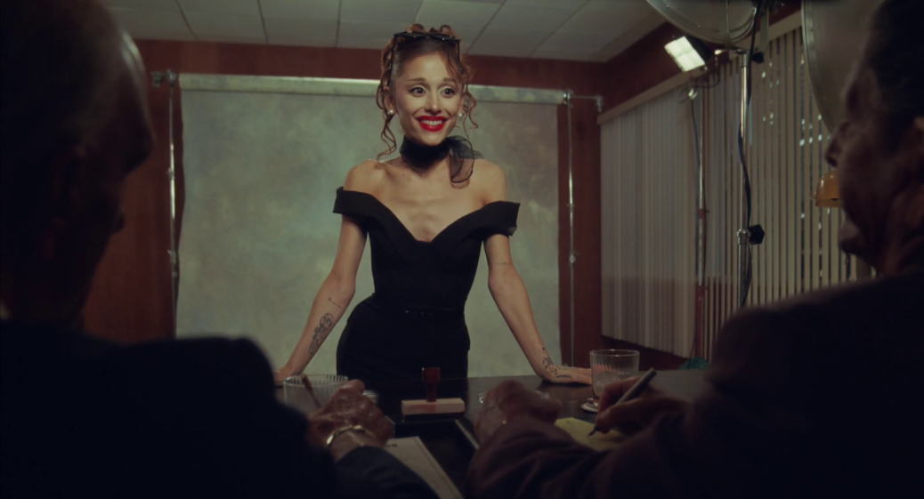 Ariana Grande smiling while leaning on a table with two men.