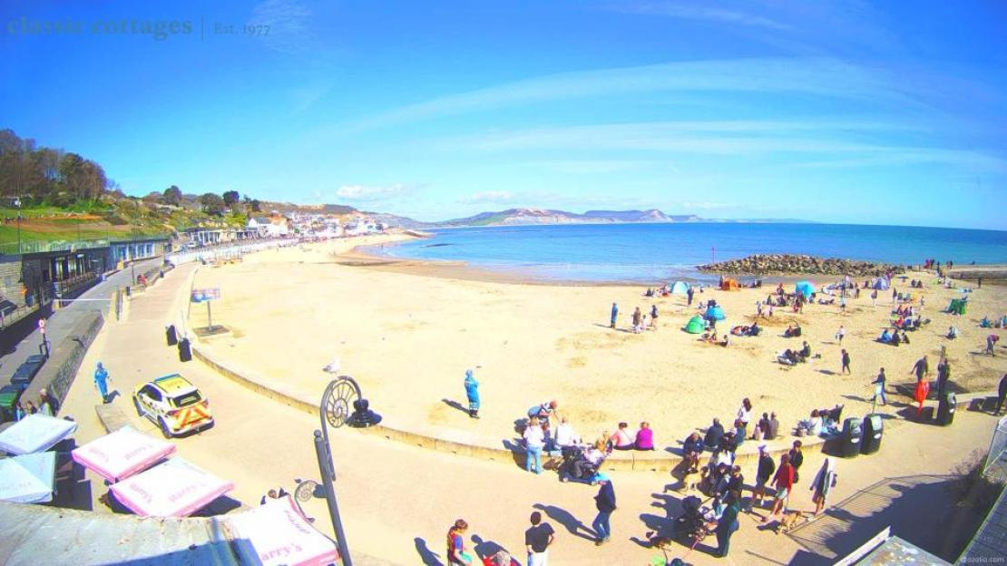 People on a sunny beach, with the ocean in the background and a town on the left.