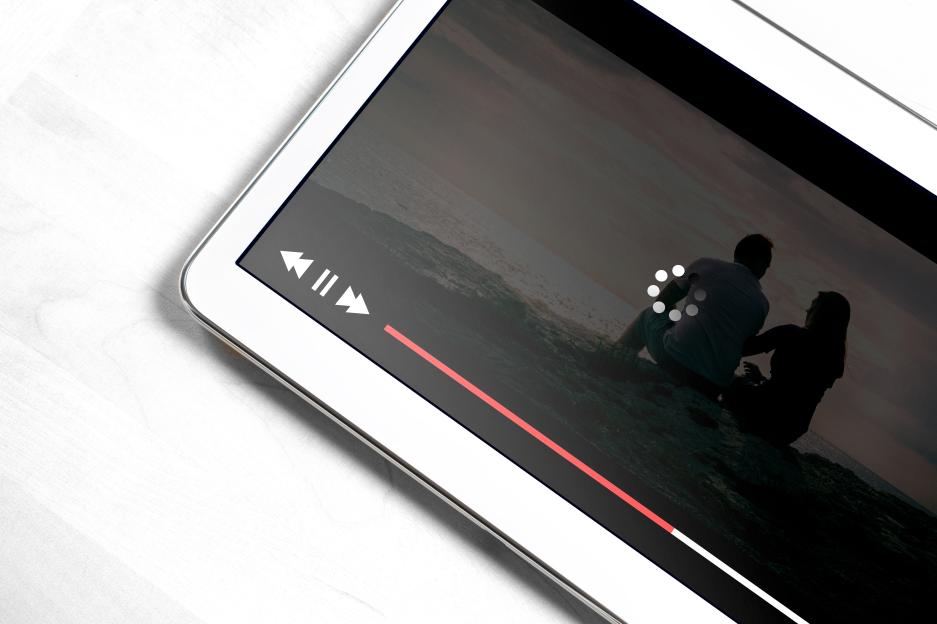A white digital tablet displaying a video player that is buffering, with a loading icon visible on the screen.
