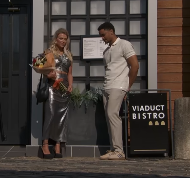 A woman in a silver outfit holding flowers stands next to a man outside the Viaduct Bistro.