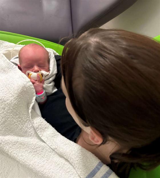 A baby, born with gastroschisis, sleeps with a pacifier while being looked over by a parent.