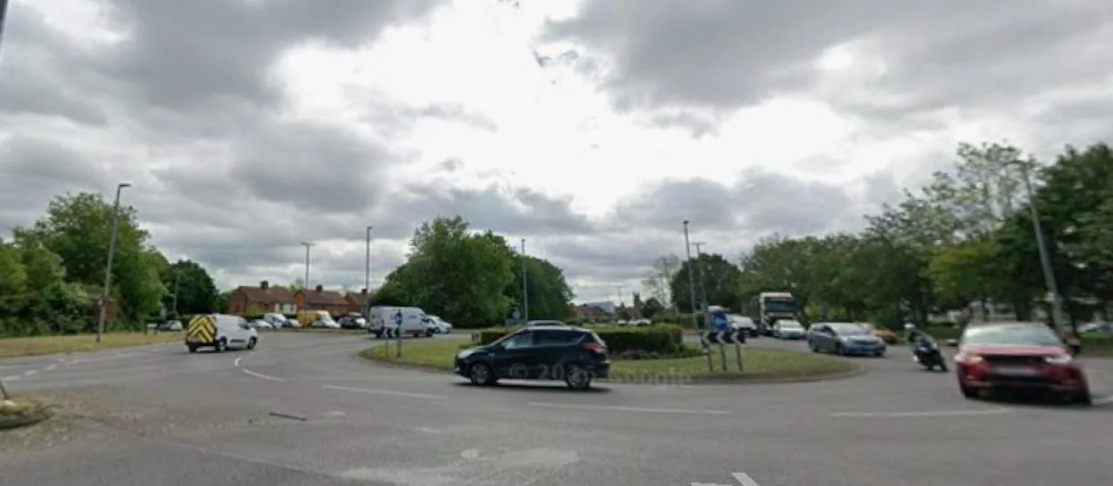 Cars driving on a multi-lane roundabout under a cloudy sky.