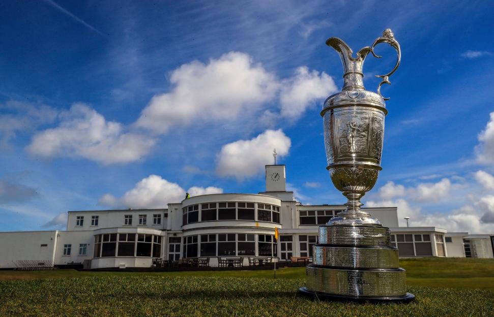 The Claret Jug golf trophy sits on green grass in front of the Royal Birkdale golf clubhouse.