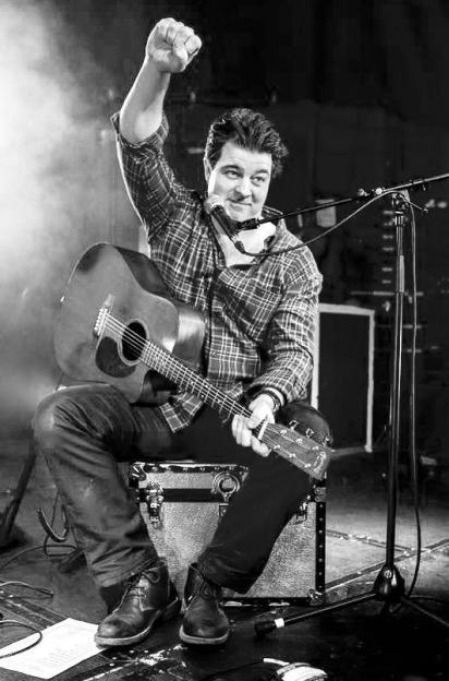 Liam Halligan raising his fist while playing guitar and harmonica.