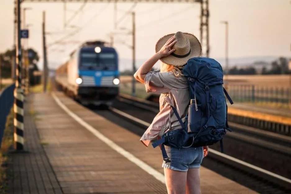 Woman with a backpack and hat looking at an arriving train.