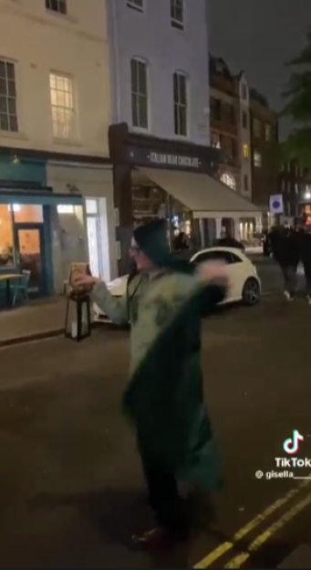 A person wearing a large green cloak swings it around on a street at night.