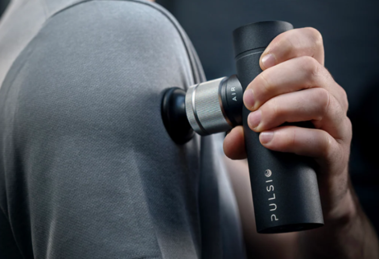 A hand holding a Pulsio percussion massager against a person's back.