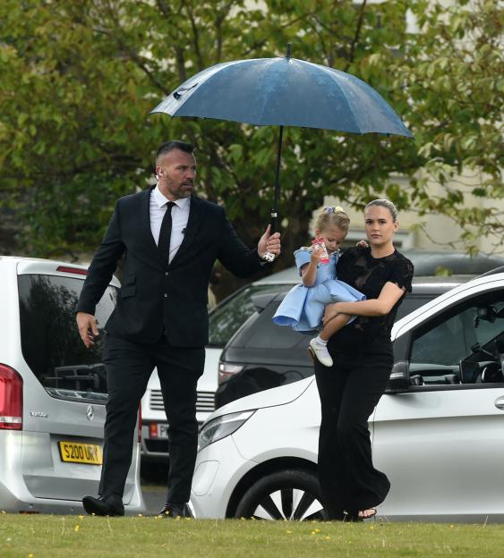 Molly-Mae Hague carrying her daughter Bambi, with a man holding an umbrella for them, at a wedding.