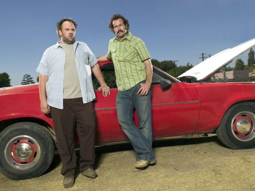Actors Ethan Suplee and Jason Lee standing next to a red car with its hood up.
