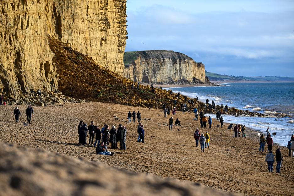 People walking on a beach after a large rock fall at East Cliff in West Bay, Dorset.