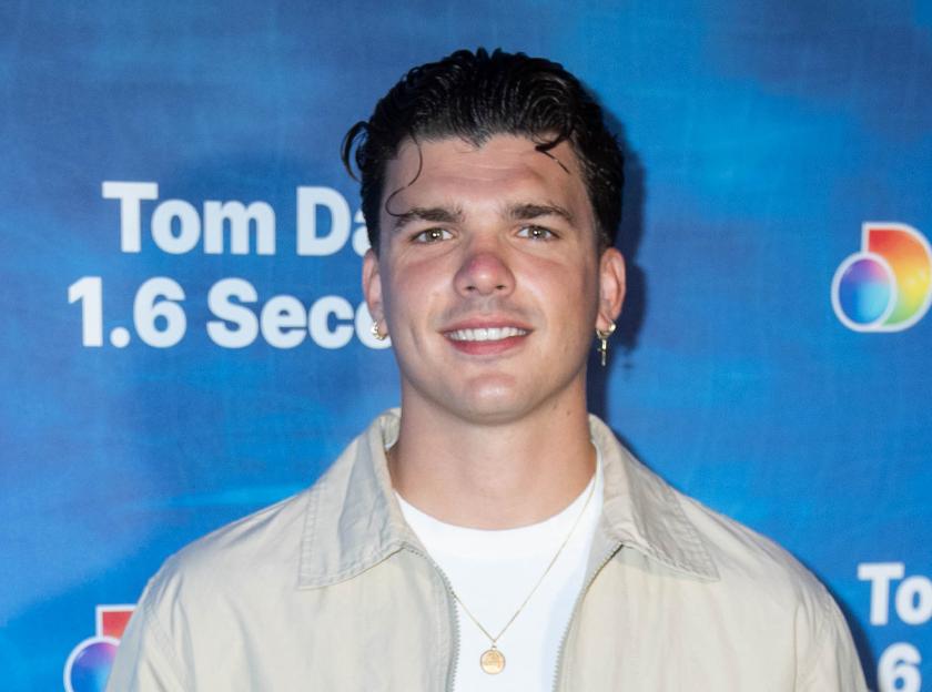 Harry Clark in a white T-shirt and tan jacket, smiling at the camera.