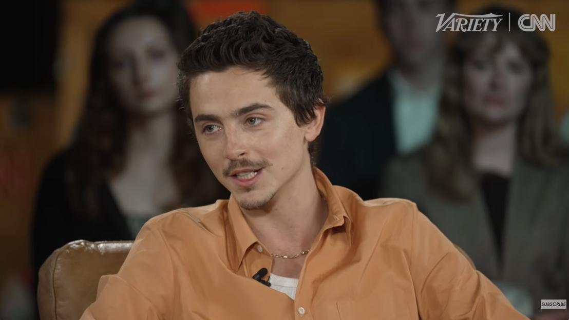 Timothée Chalamet in an orange shirt being interviewed by Variety and CNN.