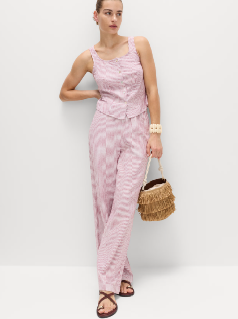 Woman in red and white striped linen trousers and matching tank top, brown sandals, and a brown fringed handbag.