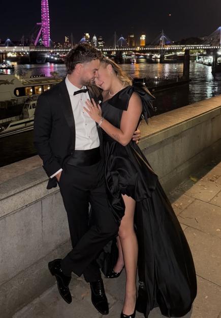 Jojo Siwa in a black thigh-split dress with Chris Hughes by the River Thames at night.