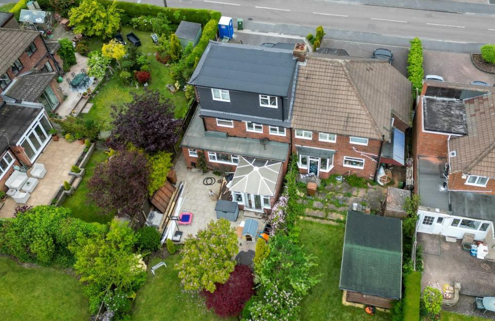 Aerial view of a house with an oversized dormer extension, visible next to similar houses and gardens.