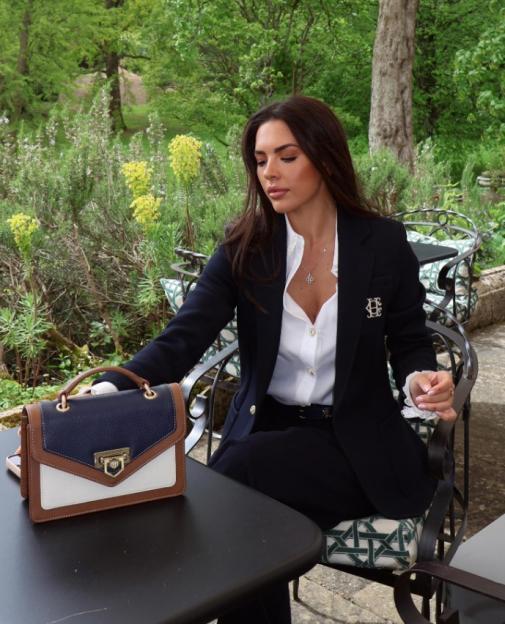 Gemma Owen in a navy suit with a white shirt, holding a color-block handbag.