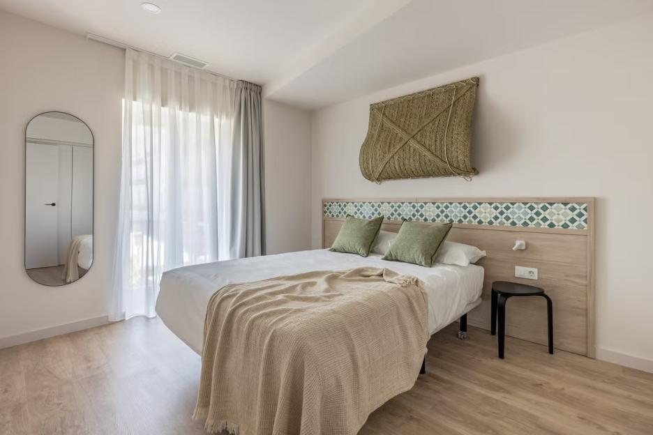 A bright bedroom with a bed, a mirror, and woven wall decor.