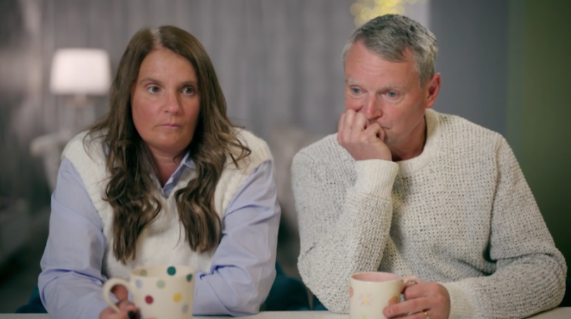 Noel and Sue Radford appearing somber while sitting at a table with mugs.
