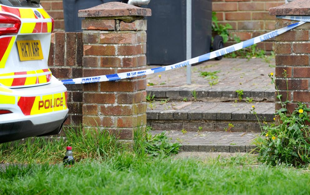 A police car is parked in front of a brick building cordoned off with blue and white police tape.