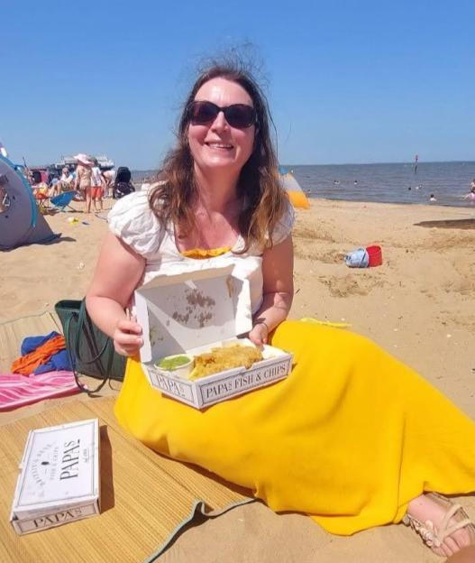 A woman in sunglasses on a beach holds a box of Papa's fish and chips.