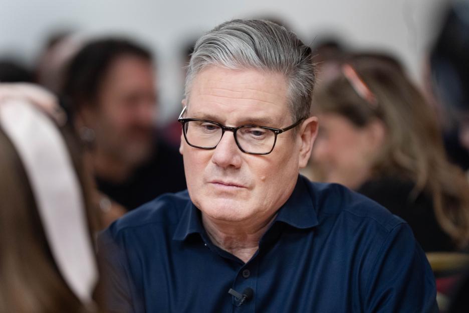 Prime Minister Keir Starmer wearing glasses and a dark blue shirt, looking down during a meeting.