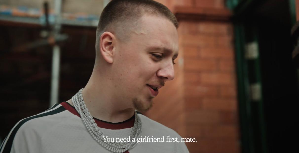 A man wearing a multi-strand diamond necklace looks right as text on the screen reads, "You need a girlfriend first, mate."