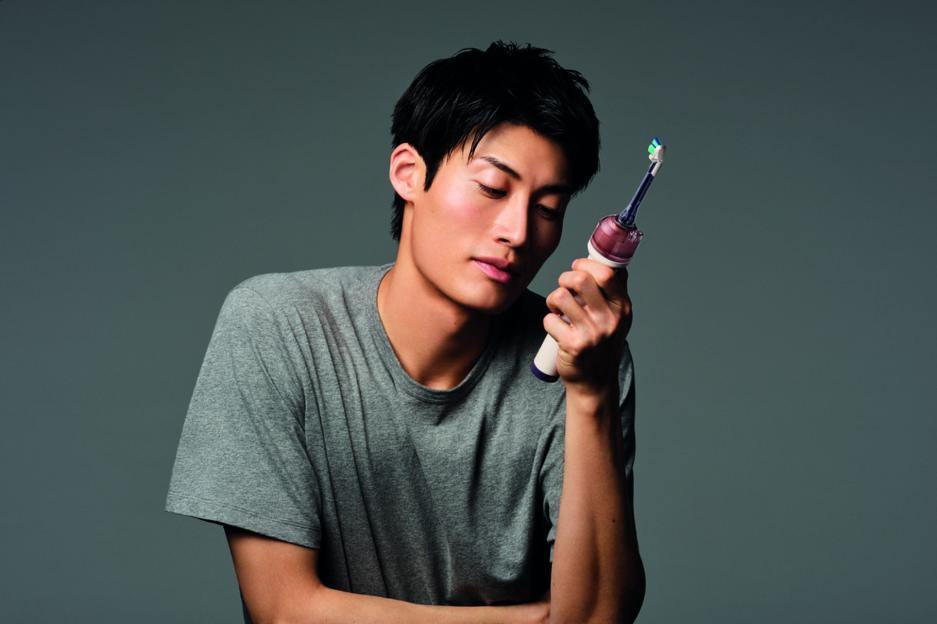 A man holding an electric toothbrush with colored bristles and a purple transparent cap, looking down at it.