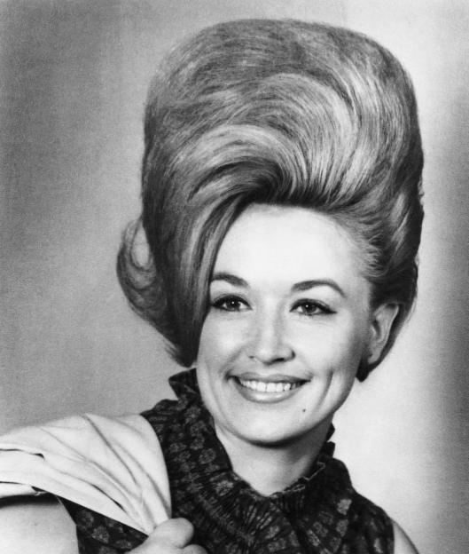 Dolly Parton with a beehive hairstyle, smiling at the camera.