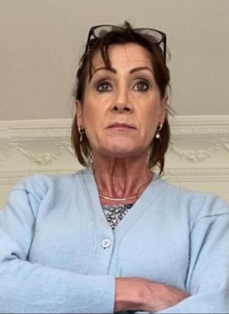 Katherine Farrimond with arms crossed, wearing a light blue cardigan and glasses on her head.
