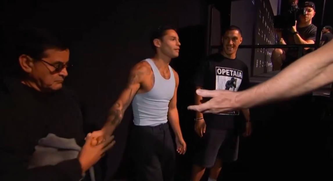 Man in a white tank top shaking hands with another man.