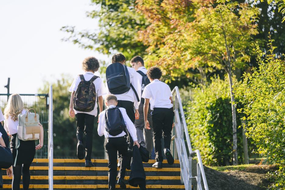 Rear view of teenagers wearing uniform and carrying bags leaving school.