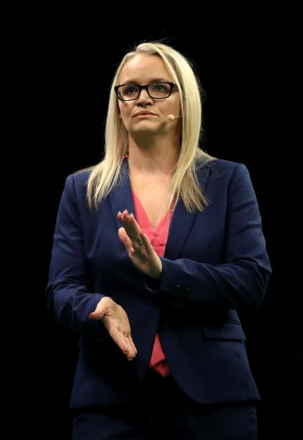 a woman wearing glasses and a blue suit is clapping her hands
