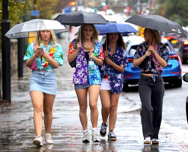 Four women in Hawaiian shirts walk with umbrellas in the rain during a pub crawl.