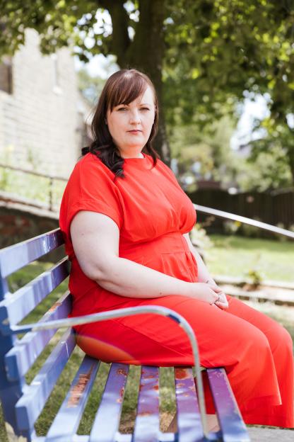 Christina O'Connor in a red dress, sitting on a blue bench.