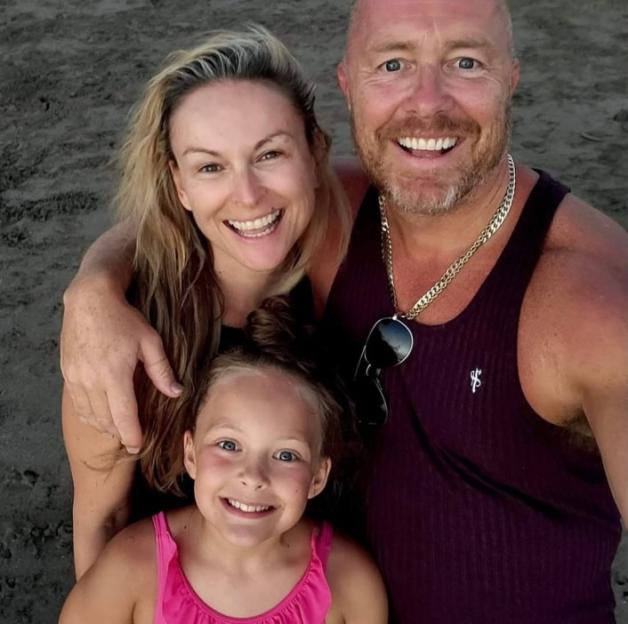 A family of three smiling for a selfie on a beach.