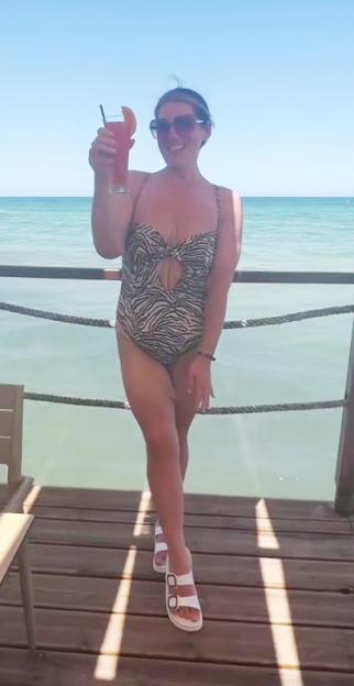 Becki Jones in a zebra print swimsuit, holding a drink, standing on a dock over water.