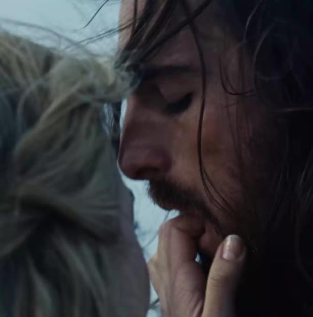 Margot Robbie touching Jacob Elordi's face, both with hair blowing in the wind.