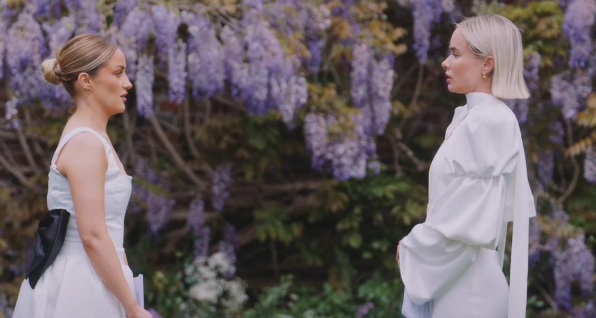 Leigh and Leah in wedding attire facing each other against a backdrop of wisteria.