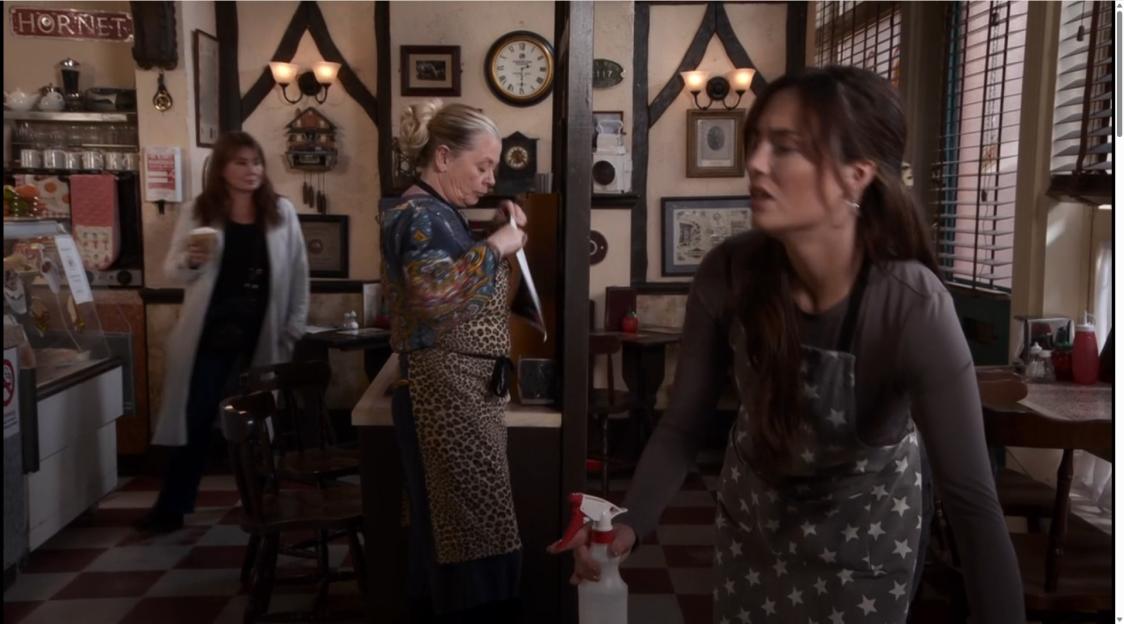 Three women in a café, two wearing aprons.