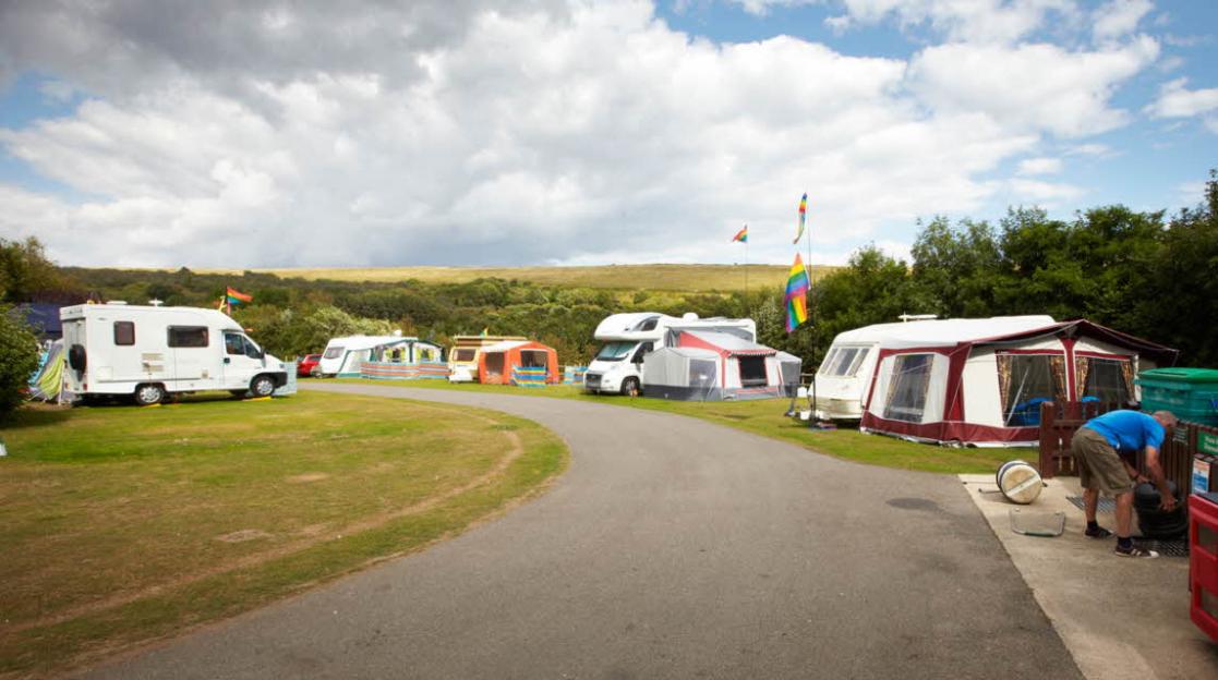 Campsite with several caravans, motorhomes, and tents under a cloudy sky.