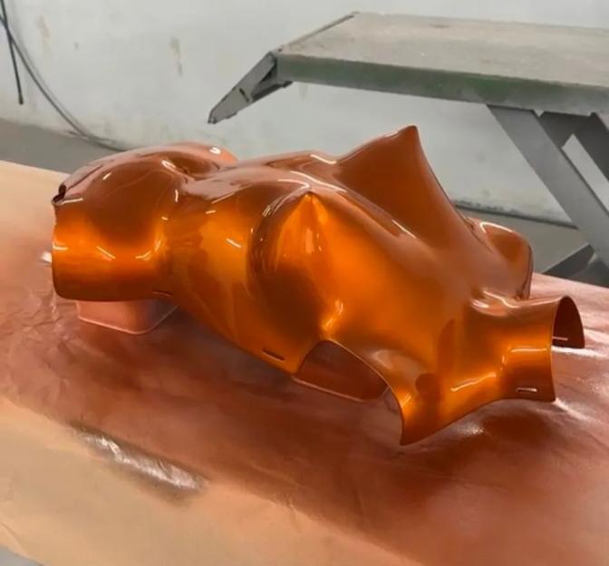 A fibreglass breastplate being painted orange at a body shop.