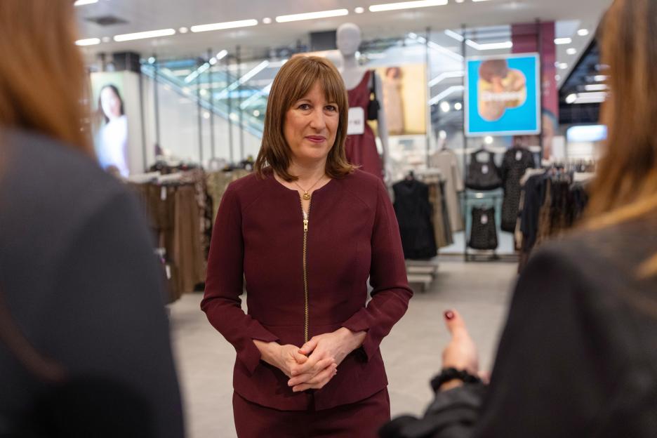 Chancellor of the Exchequer Rachel Reeves in a burgundy suit speaking to someone in a retail store.