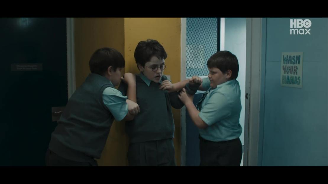 Two boys holding a third boy against a yellow wall in a school hallway.