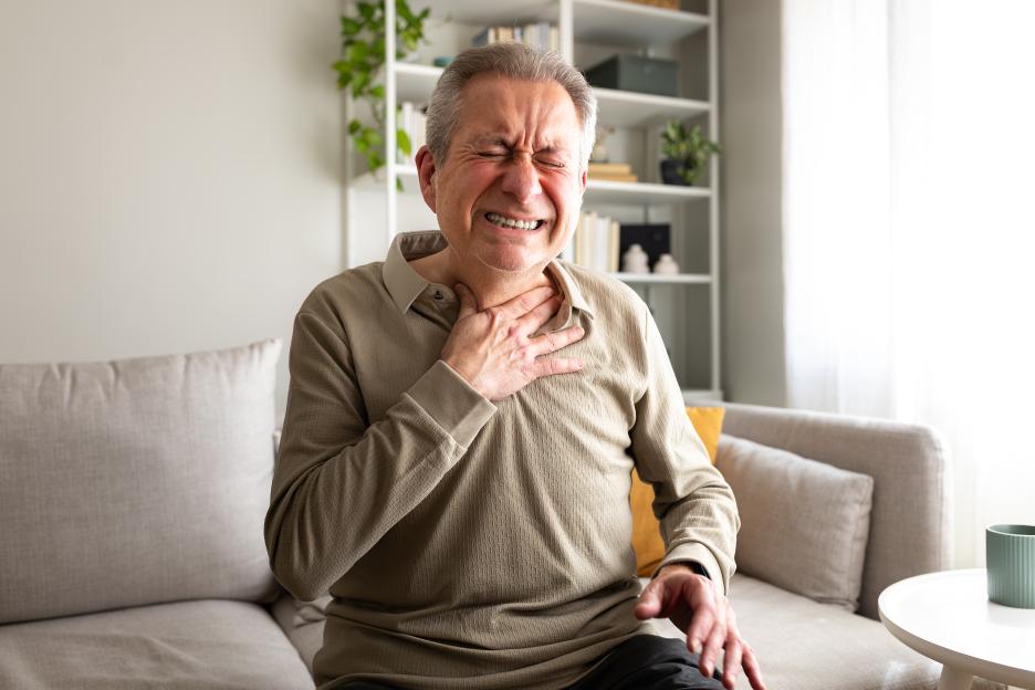 Senior man suffering from chest pain while sitting on a sofa at home.