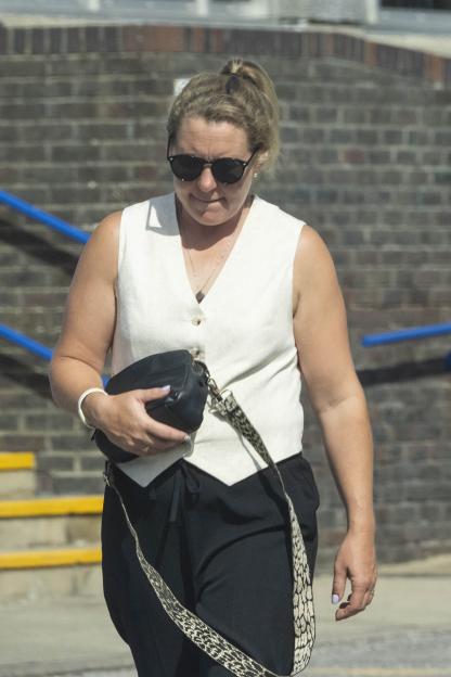 Sophie Tuffin, a woman with blonde hair tied in a ponytail and wearing sunglasses, a white vest top, and black trousers, walking while holding a black purse.