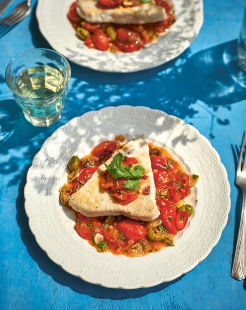 Tuna steak with tomatoes and herbs on a white plate.